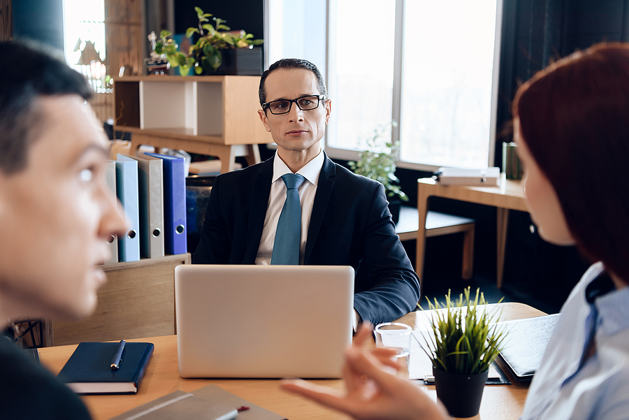 Male attorney in a suit sitting in front of a couple  going through a divorce with his laptop open. 