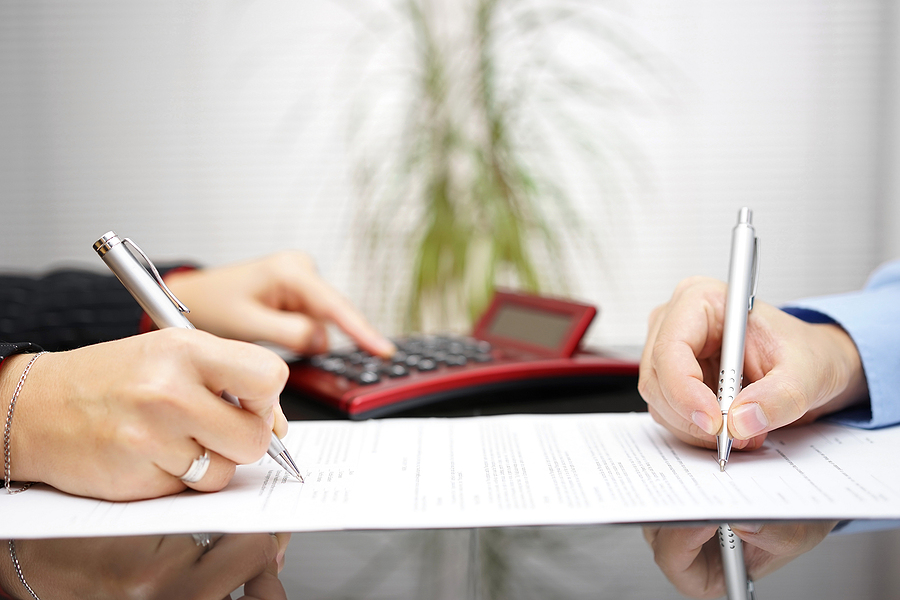 Close up of a couple's hand going over financial documents with a pen and paper in hand and a calculator. 