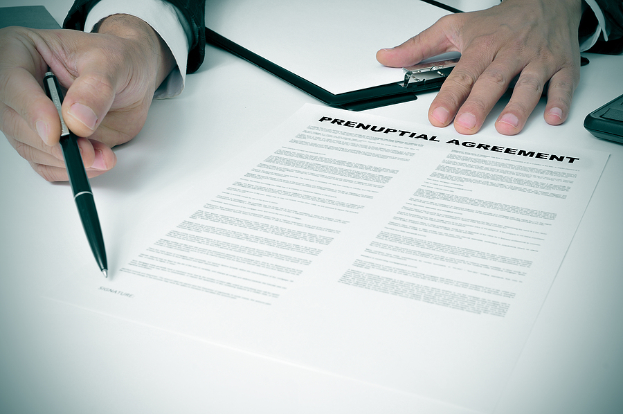 Close up of a man wearing a suit and holding a pen to a prenuptial agreement. 